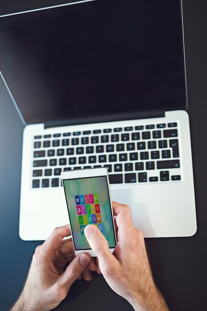 A person's hand holding a smartphone displaying various social media apps and marketing icons, with a blurred laptop in the background showing analytics, illustrating digital marketing efforts.